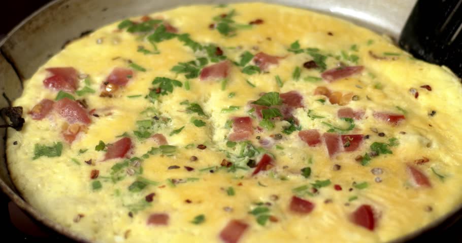 An egg with greens and spices in a frying pan is cooked on a gas stove, natural and delicious food.