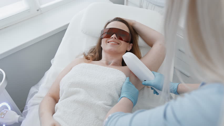 A professional cosmetologist performs laser hair removal in a cosmetology salon. Woman cosmetologist removes body hair. Professional aesthetic skin care in a beauty clinic. Smooth and soft skin hands  | Shutterstock HD Video #1101937669
