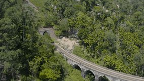 Drone aerial view: Red train moving on railroad ancient nine arch bridge in Ella, Sri Lanka. Famous tourist attraction