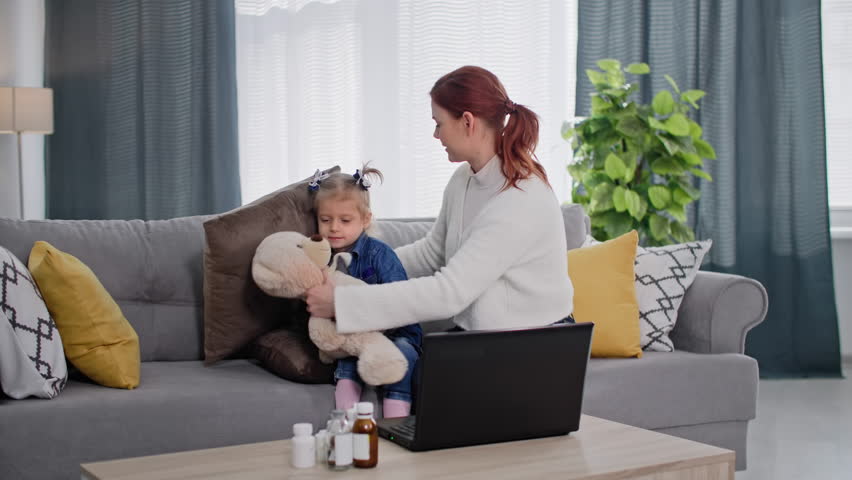 Illness of a child, a loving mother persuades a female kid to take medication from observation after consulting a doctor online via video link on a laptop while sitting on a sofa in room | Shutterstock HD Video #1101941513