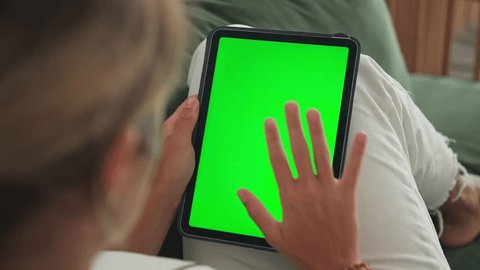Girl click green screen display. Hand hold vertical ipad close up. Finger tap center tablet job. View green web store site. One touch chroma key pad. Woman poke screens. Person work home room lie sofa Adlı Stok Video