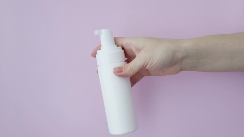 Facial foam dispenser, face wash, cleansing cosmetics in a woman's hand on pink background | Shutterstock HD Video #1101944283