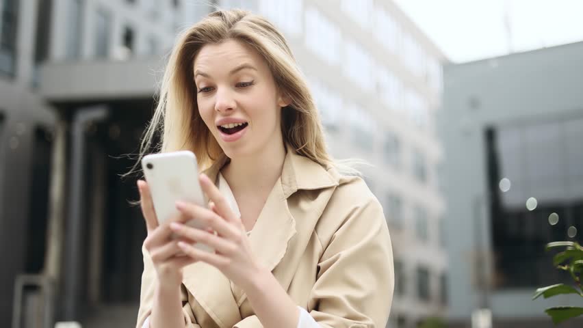 Portrait of young blond woman looking at smartphone cellphone screen with nod of approval and looking at camera pointing at the phone near business centre Advise Approve Recommend Choice concept | Shutterstock HD Video #1101945713
