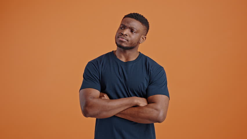 Confused dark-skinned man with his arms folded, looking at camera with stupefaction, astonishment and disappointment, pointing at himself and asking what, isolated orange background. People. Emotions Royalty-Free Stock Footage #1101947853