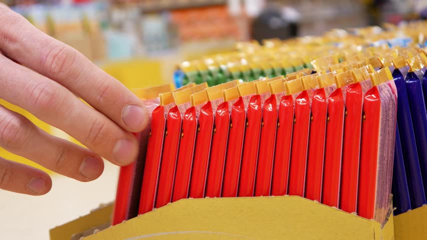 Close-up of many colorful chocolate bars standing in rows and a male buyer's hand takes one