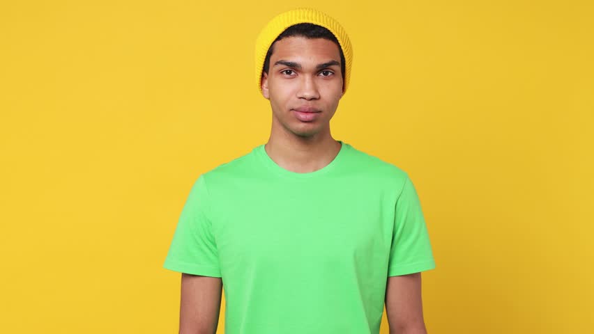 Young smiling happy cheerful kind friendly man of African American ethnicity wearing basic green t-shirt hat look camera isolated on plain yellow background studio portrait. People lifestyle concept Royalty-Free Stock Footage #1101954021