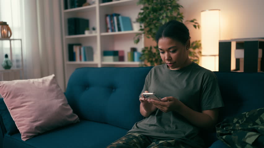 Little son with ball hugging military mother, woman looking for job on gadget