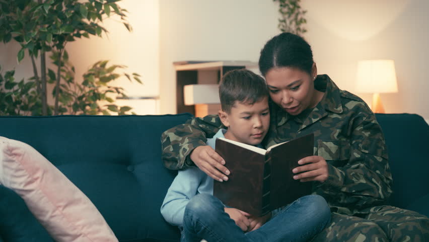 African American woman in military uniform reading book together with little son