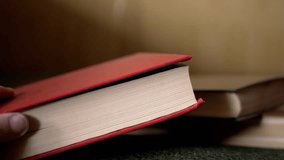 Hands Open a Thick Red Book Turning through it against a Blurred Background. Turning the pages of a book. Reading at home. Home library. Mysterious atmosphere. Weak lighting. Stack of books. Close-up. - Powered by Shutterstock - Get 15% off with code: PIKWIZARD15