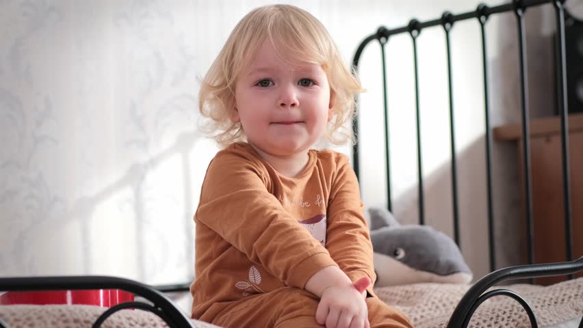 Little beautiful girl sits on the bad in the room and plays