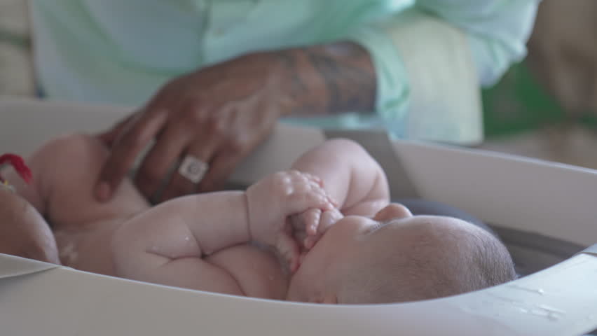 Baby bath time, father pours water carefully on newborn cheek, Caucasian white family