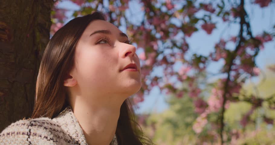 Girl Leisurely Sitting Under The Tree While Looking On Cherry Blossom Flowers In Paris, France. - close up, side view