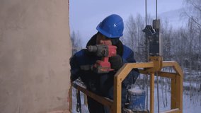 Builder in uniform drills hole in wall. Clip. Repairman makes hole with drill. Builder with drill makes hole