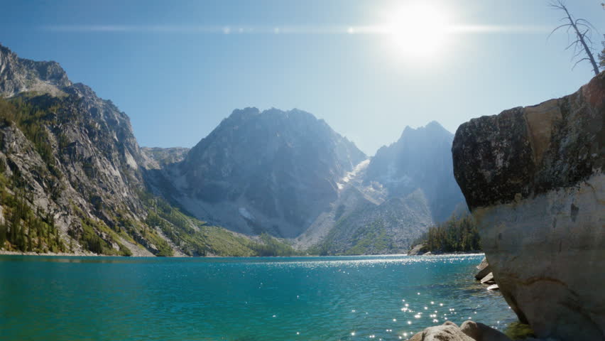 Hiker Walks to Rock Edge for View of Turquoise Alpine Lake. Adventurous Man Standing at a Lookout Viewpoint Taking in Breathtaking Scenery at Colchuck Lake in Leavenworth Washington
