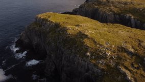 Aerial East Coast revealing shot of waves crashing on high rocky cliffs at Spillars Cove Twillingate Newfoundland Canada.
