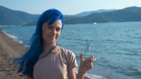 Cut off hair. Girl with scissors. A cute girl with blue hair holds scissors in her hands against the backdrop of the sea.