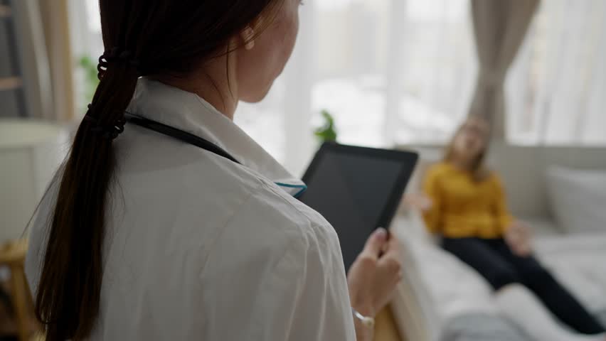 Female doctor holding using digital tablet in house patient. Girl with broken leg in cast. Woman physician listens to complaints and writes it on pad computer. Modern healthcare technology concept. | Shutterstock HD Video #1101975107