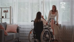 Cheerful blonde woman talks to girlfriend with disability in wheelchair gently touching chin. Happy LGBT couple enjoys spending time together in apartment - Powered by Shutterstock - Get 15% off with code: PIKWIZARD15