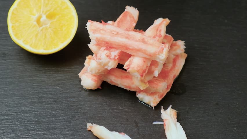 The girl successively picks up a piece of crab meat snack until there is nothing left on the cutting board. Close-up.