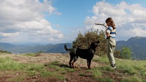 Girl plays with stick with dog-Rottweiler on cliff of mountain in valley of Rhodope Mountains