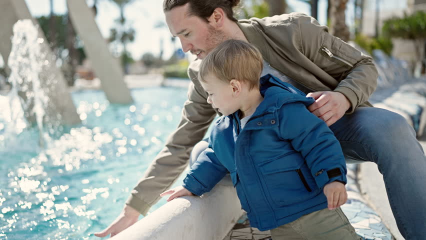 Father and son smiling confident playing with water at park
