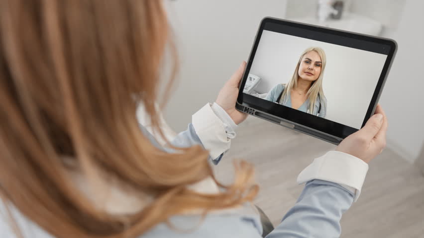 Therapist cardiologist provide medical heart disease consultation to client by video call, laptop screen view over patient shoulder sit at desk got help from woman practitioner doctor in white coat | Shutterstock HD Video #1101983245