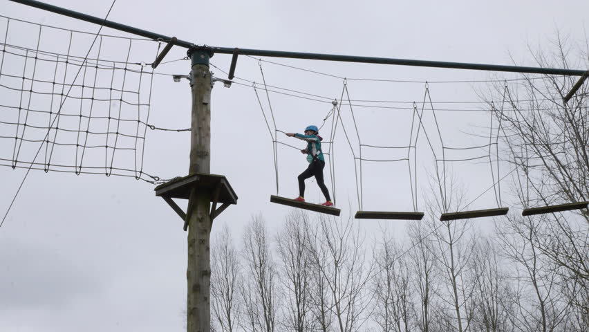 Girl walking across planks on ropes on a high wire adventure obstacle course | Shutterstock HD Video #1101985455