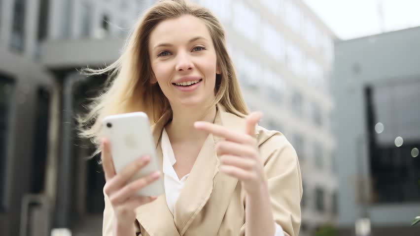 Portrait of young blond woman looking at smartphone cellphone screen with nod of approval and looking at camera pointing at the phone near business centre Advise Approve Recommend Choice concept | Shutterstock HD Video #1101987951