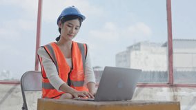 Asian female engineer doing online video conference from construction site. Wearing protective gear such as safety helmets and reflective vests. in the construction area. 