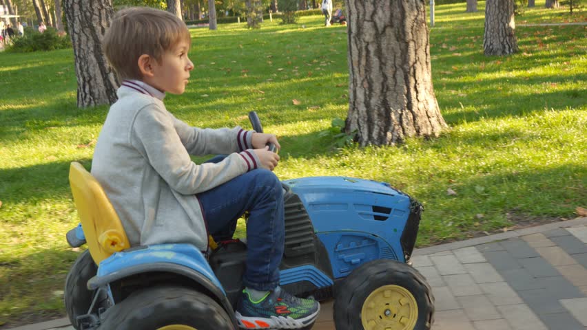 Happy boy riding on toy tractor at park. Kids playing in park, farming, driving transport. Royalty-Free Stock Footage #1101991541