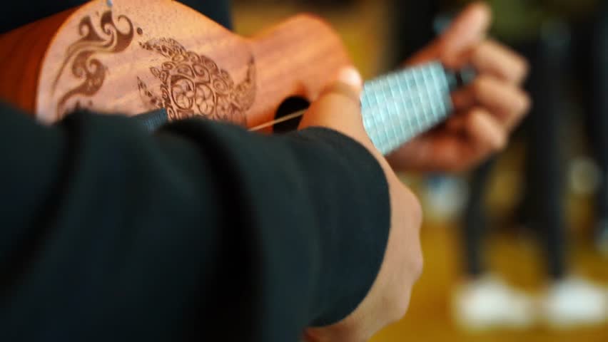 Boy in a black sweater plays single simple chords on a wooden ukulele close-up