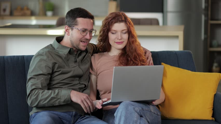 Happy couple laughing talking making distance video call looking at laptop webcam sitting on sofa, enjoy online chat internet conversation on at home. distance friends chatting online in virtual app e | Shutterstock HD Video #1101998653
