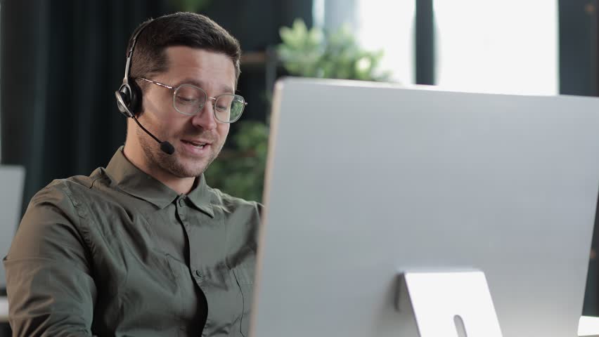 Focused young businessman in eyewear wearing headphones, holding video call with clients on laptop. Concentrated millennial man in glasses giving online educational class lecture, consulting customer | Shutterstock HD Video #1101998693