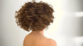 Attractive young female model, with curly afro hair, looking at the camera while playing with her hands on her head. Caucasian woman with bare shoulders - Powered by Shutterstock - Get 15% off with code: PIKWIZARD15