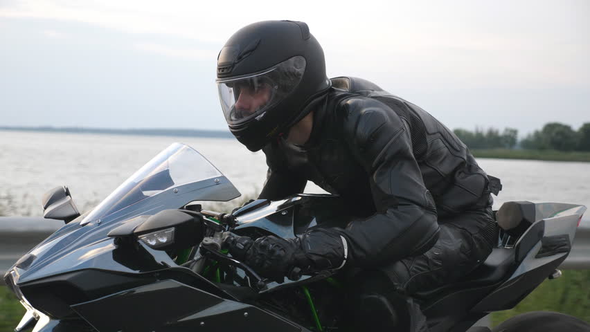 Close up of biker driving motorbike during road trip near river or lake. Man ride fast on modern sport motorcycle at country road. Motorcyclist racing his bike on rural route. Concept of adventure
