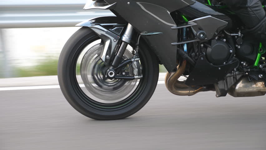 Wheel of modern sport motorbike riding fast at highway. Motorcycle driving at asphalt route. Motor bike racing on country road. Concept of freedom and adventure. Close up Slow motion Side view