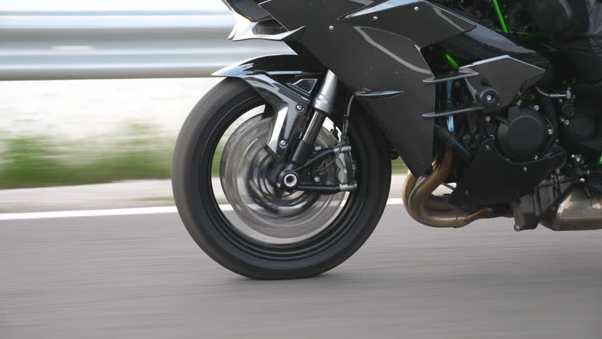 Wheel of modern sport motorbike riding fast at highway. Motorcycle driving at asphalt route. Motor bike racing on country road. Concept of freedom and adventure. Close up Slow motion Side view