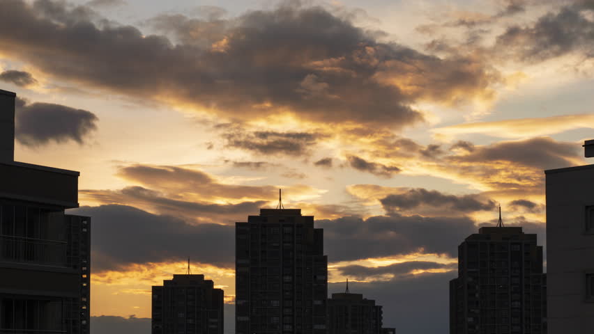 An impressive sunset view from behind the lights of the city and buildings. Dance of the clouds above the buildings. Cloud movements and city lights taken with time lapse technique. Royalty-Free Stock Footage #1102000177