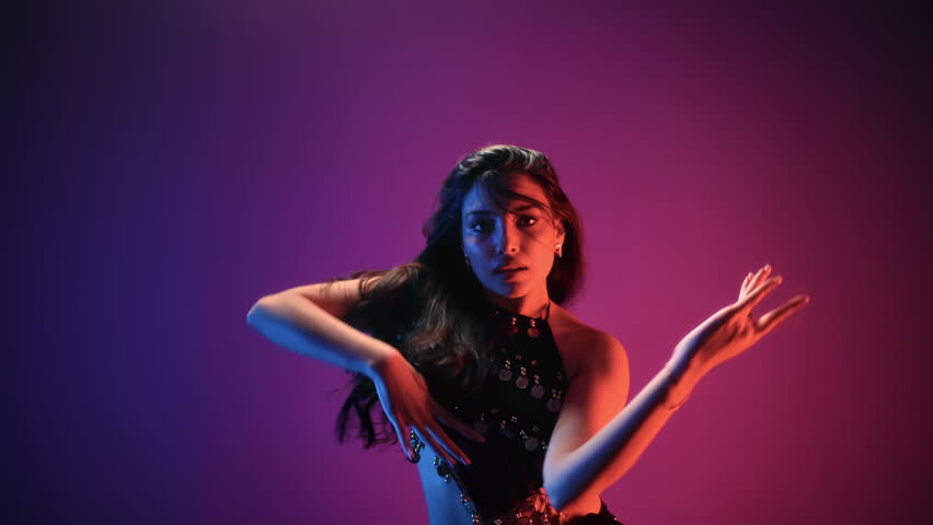 Graceful Asian woman belly dancer plastic flex movement performance posing at dark neon backlit studio slowmo. Arabic artist female dancing ethnic culture show body dress sequins rhinestones jewelry