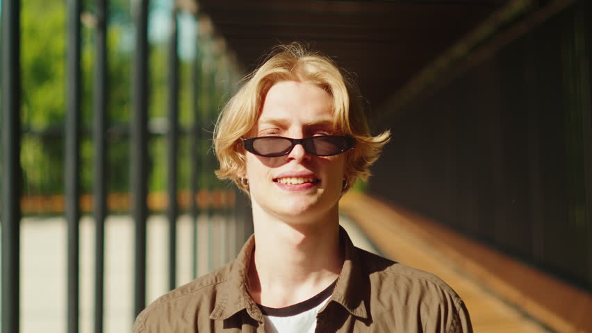 Young man portrait. Happy male student smiling close-up. Cheerful guy posing outdoor, model wearing sunglasses, looking at camera.