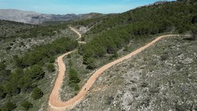 A female cyclist is riding her gravel bicycle on a gravel road between mountains.Sport cycling motivation drone video.Riding the spanish gravel roads.Castell de Castells, Alicante, Spain.