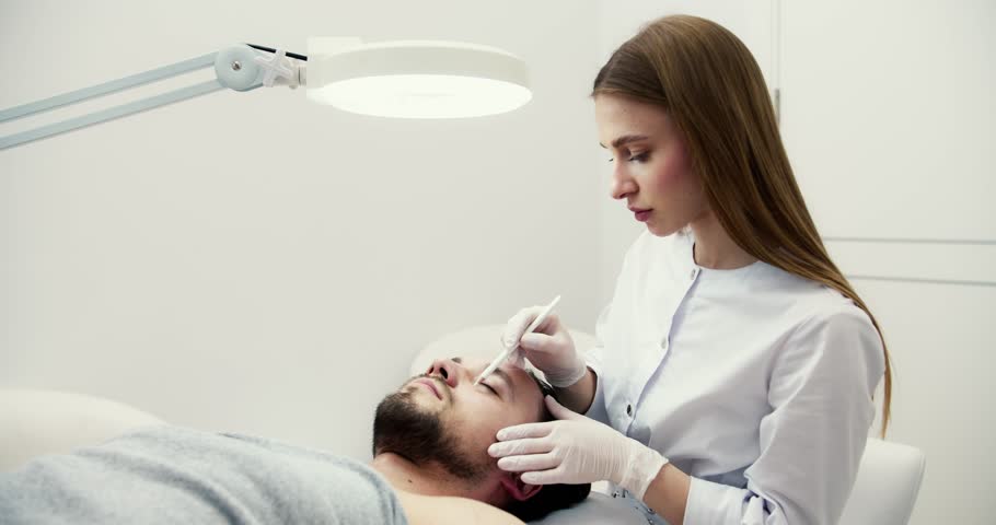 Doctor making marks on male face, handsome bearded man on consultation at surgeon or beautician | Shutterstock HD Video #1102003589