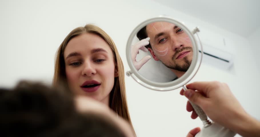 Handsome caucasian man on consultation at surgeon or beautician with contouring on face looking to the mirror | Shutterstock HD Video #1102003615