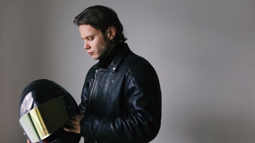 male motorcyclist biker in a leather jacket puts on a helmet.