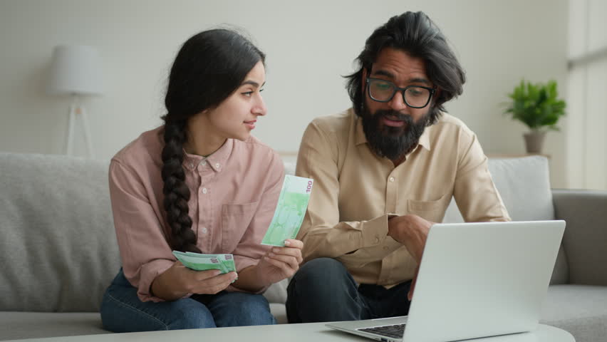 Wife and husband planning budget arabian muslim couple count money at home distribute currency two piles rich woman man counting euro banknotes cash on table with laptop online paying bank loan credit | Shutterstock HD Video #1102005029