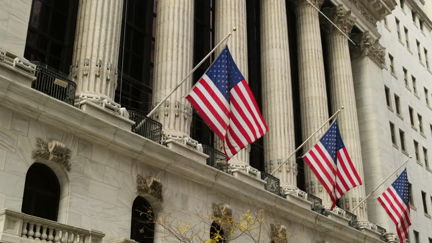 Famous Wall street and the building in New York, New York Stock Exchange with patriot flag. Wall Street road sign in the corner of New York Stock Exchange. New York Stock Exchange