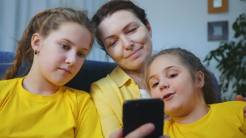 Happy family at home children mom use mobile phone for leisure. Mom sitting at home on couch watching cartoon phone.Use mobile for leisure communication while sitting home. Happy family with children. | Shutterstock HD Video #1102012041