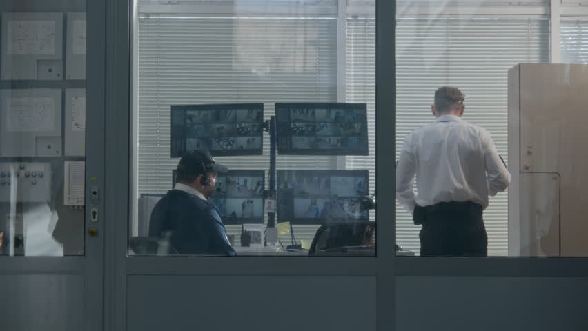 Security worker watches out window through blinds in observation room. Then monitors CCTV cameras displayed on computer screens together with coworker. Observation and tracking system. Social safety. | Shutterstock HD Video #1102015493