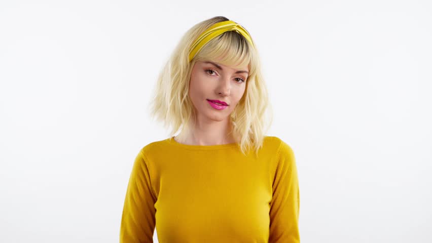 Woman sends air kiss smiling looking at camera. Happy positive emotional blonde girl. Joyful cheerful pretty lady in yellow sweater, smile face. Indoors studio, isolated on white background | Shutterstock HD Video #1102016461