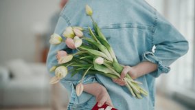 Young girl with gift and flowers bouquet behind back prepares to give it grandparents, back view. Granddaughter gives presents to senior couple granny and grandpa. They hug and kiss her at home. - Powered by Shutterstock - Get 15% off with code: PIKWIZARD15